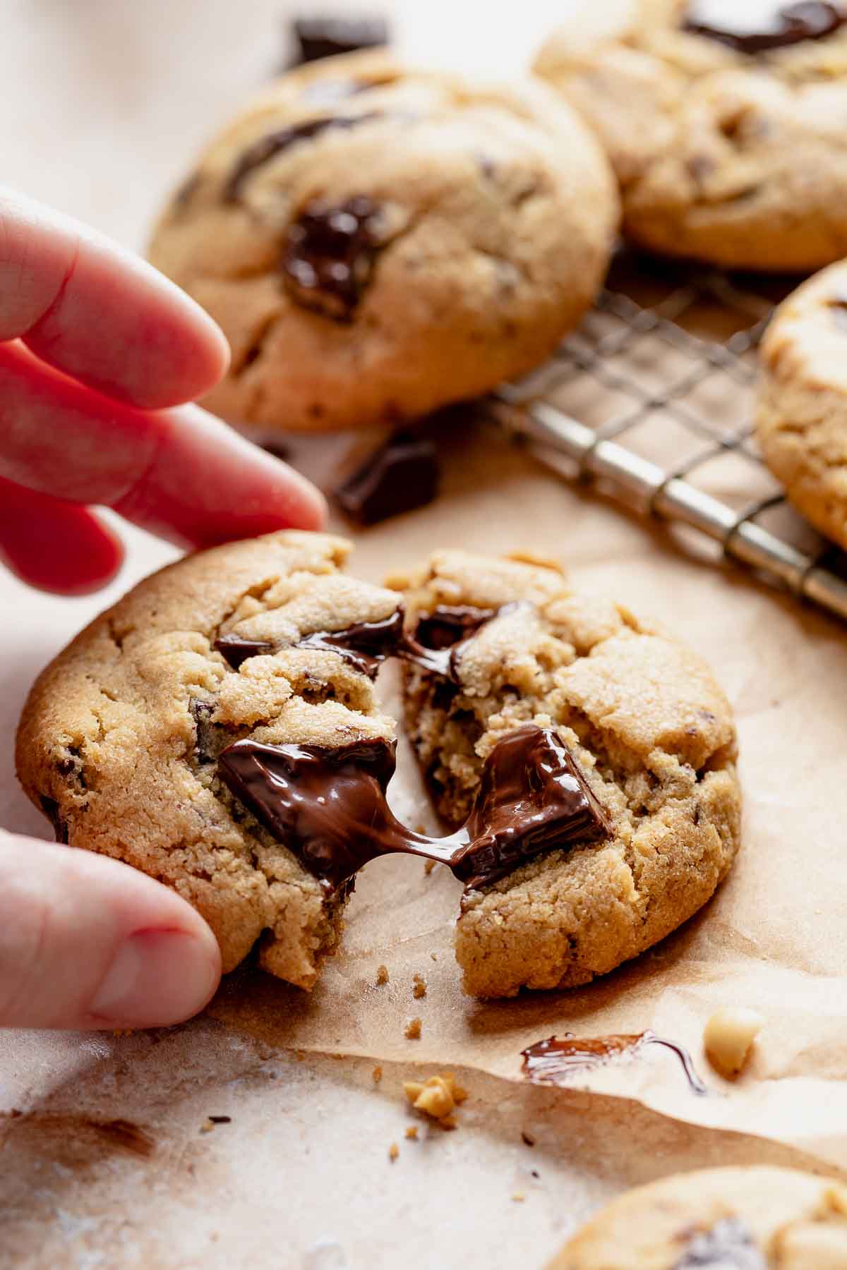 Hand pulling apart a chocolate chip peanut butter cookie with melted chocolate chunks.