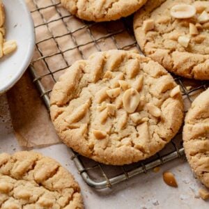Baked peanut butter cookies on a cooling rack with chopped peanuts on top.