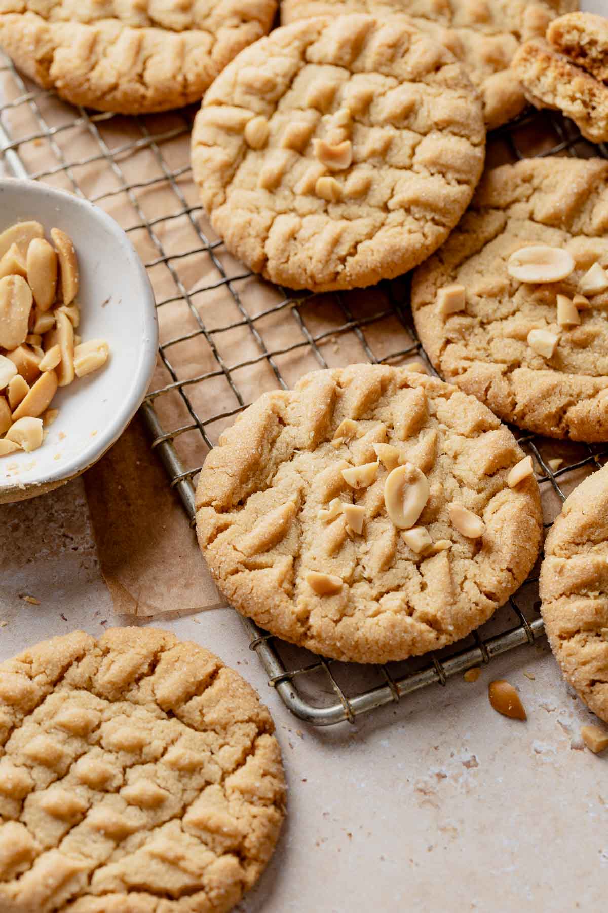 Several gluten-free peanut butter cookies cooling on a wire rack beside a dish of peanuts.