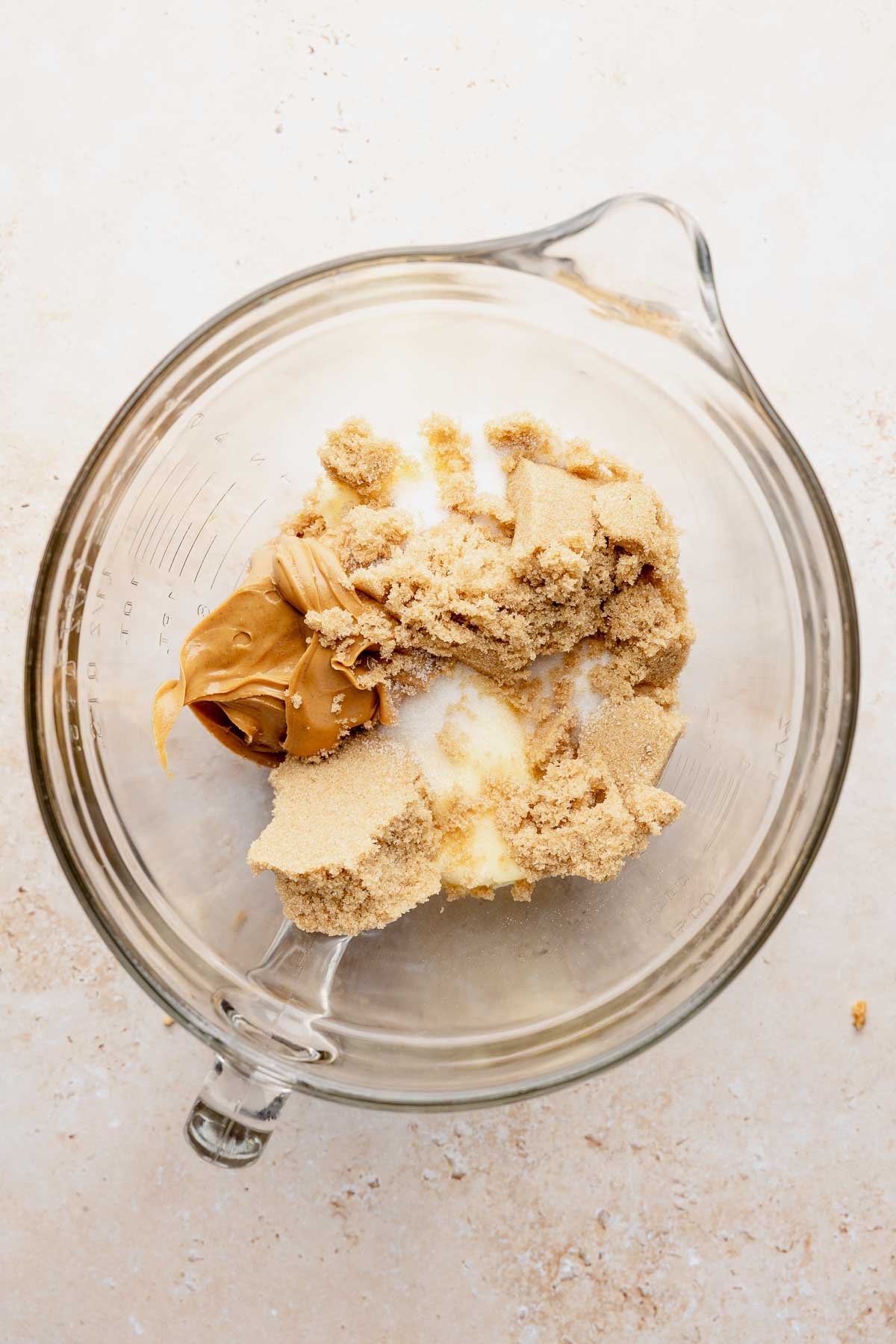 Butter, sugars, and peanut butter combined in a glass mixing bowl.