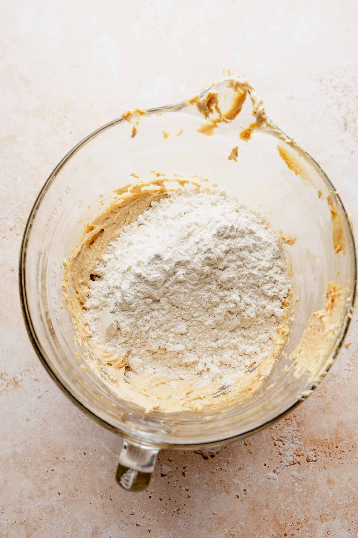 Gluten-free flour added to peanut butter cookie dough in a glass mixing bowl.