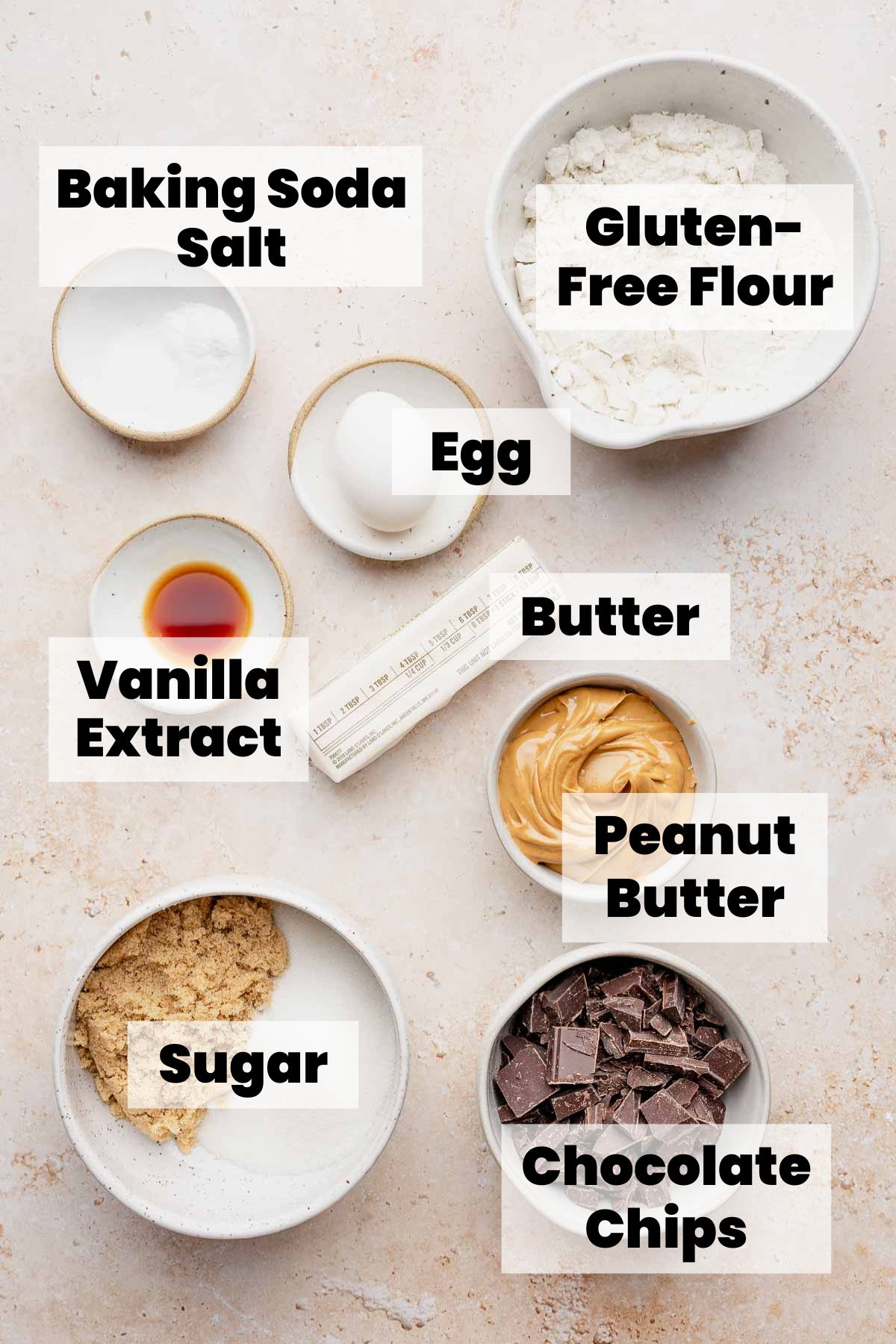 Bowls of labeled ingredients: peanut butter, chocolate chips, gluten-free flour, sugar, egg, butter, vanilla, baking soda, salt.