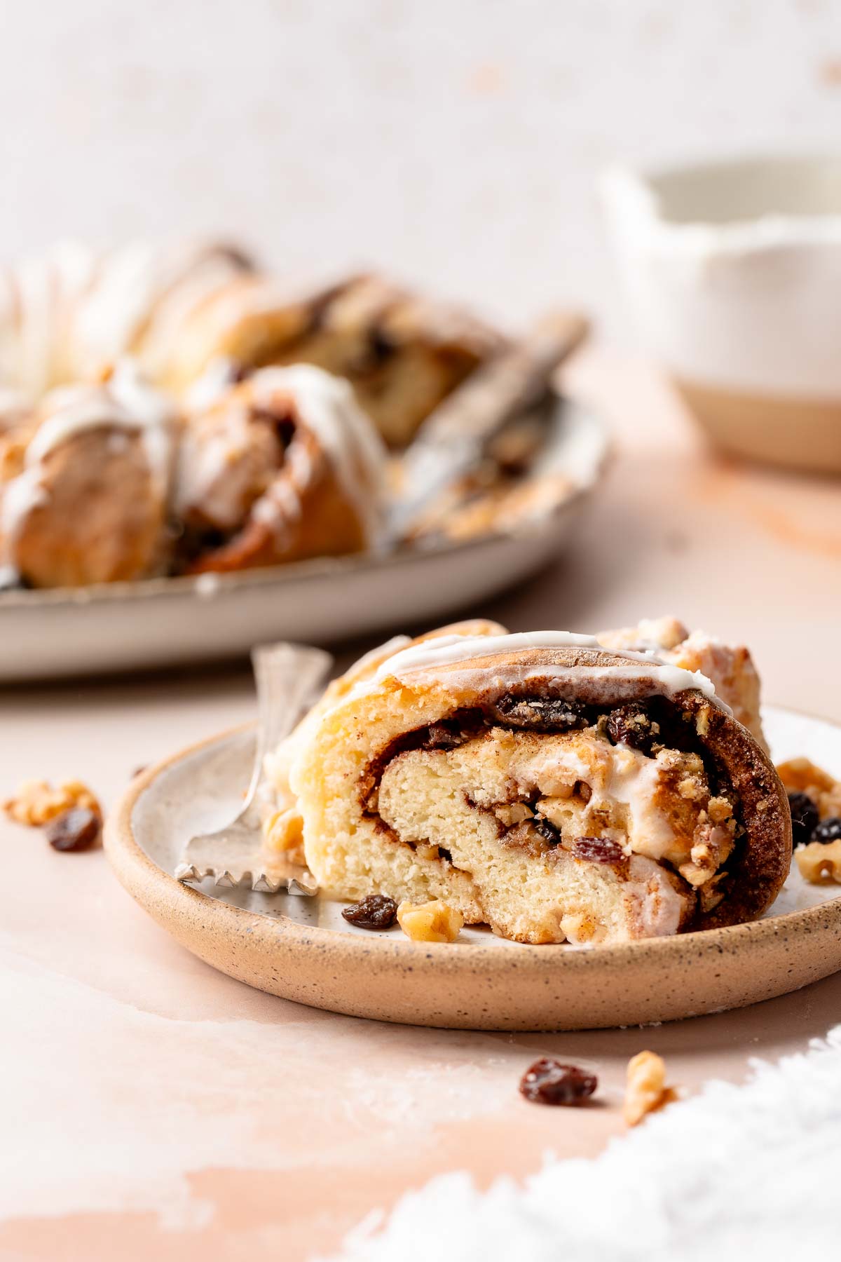 Slice of gluten free Swedish tea ring with icing, raisins, and walnuts on a plate.