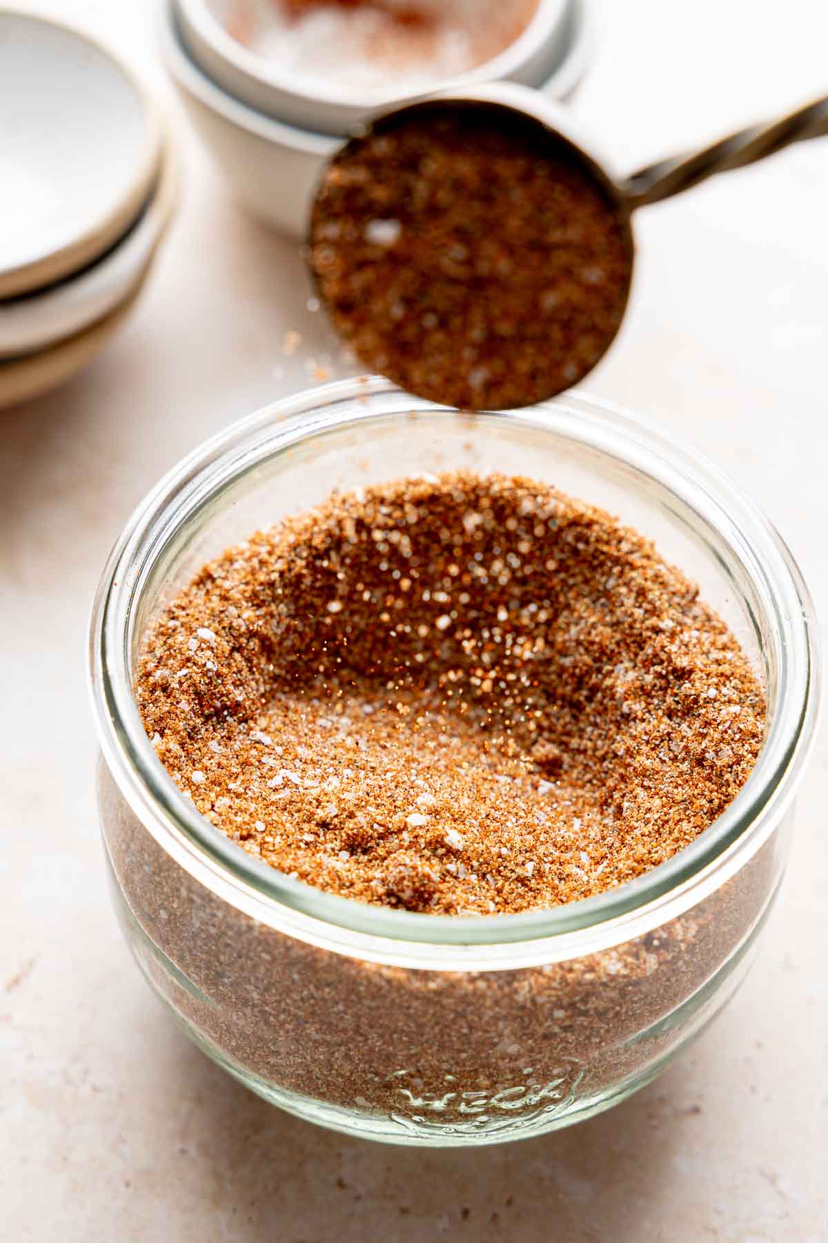 Homemade bbq seasoning pouring from tablespoon into jar filled with seasoning.