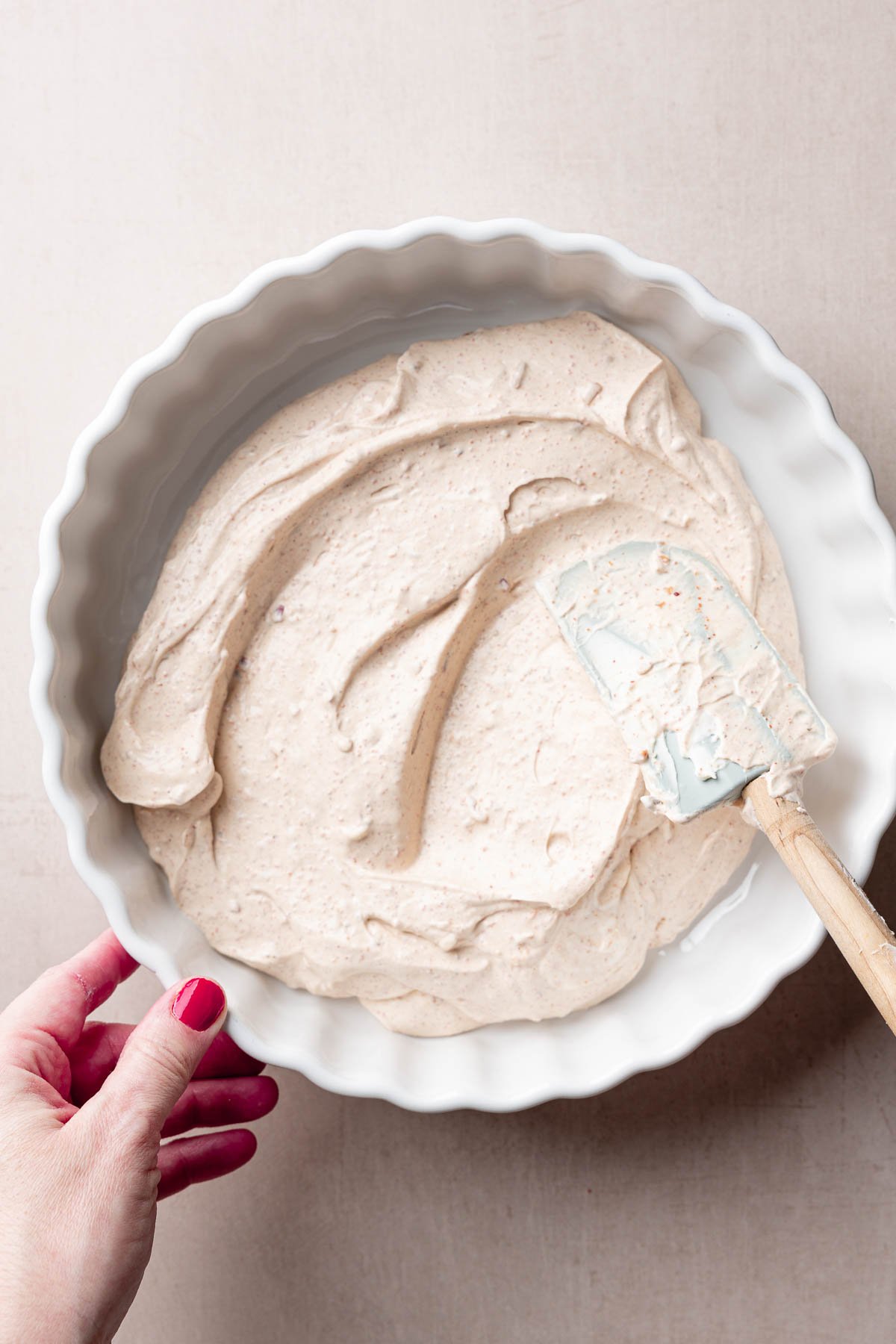 Spatula spreading cream cheese taco dip base into casserole dish.