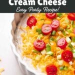 A white casserole dish layered with cream cheese taco dip base, cheddar cheese, orange bell pepper, and green onion.