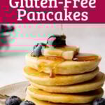 A stack of gluten free pancakes with a pat of butter, blueberries, and syrup drizzled over the top.