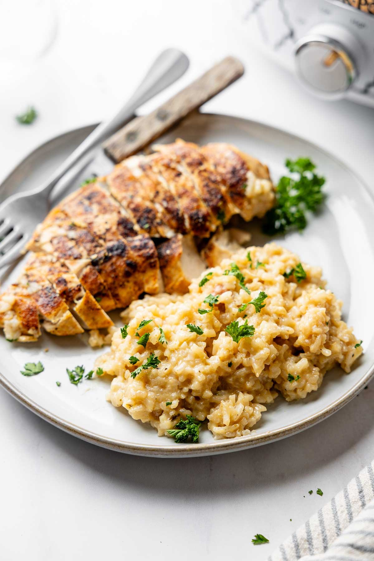 A plate with a serving of rice garnished with parsley next to a sliced chicken breast, fork and knife.