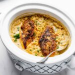 Golden brown chicken breasts on top of creamy rice inside 3 quart slow cooker.