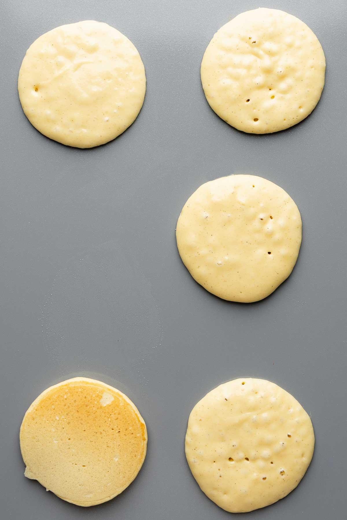 Gluten-free pancakes on a griddle, with bubbles on surface before being flipped.