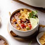 Bowl of chicken tortilla soup garnished with tortilla chips, lime wedges, and cilantro.