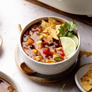 Bowl of chicken tortilla soup garnished with tortilla chips, lime wedges, and cilantro.