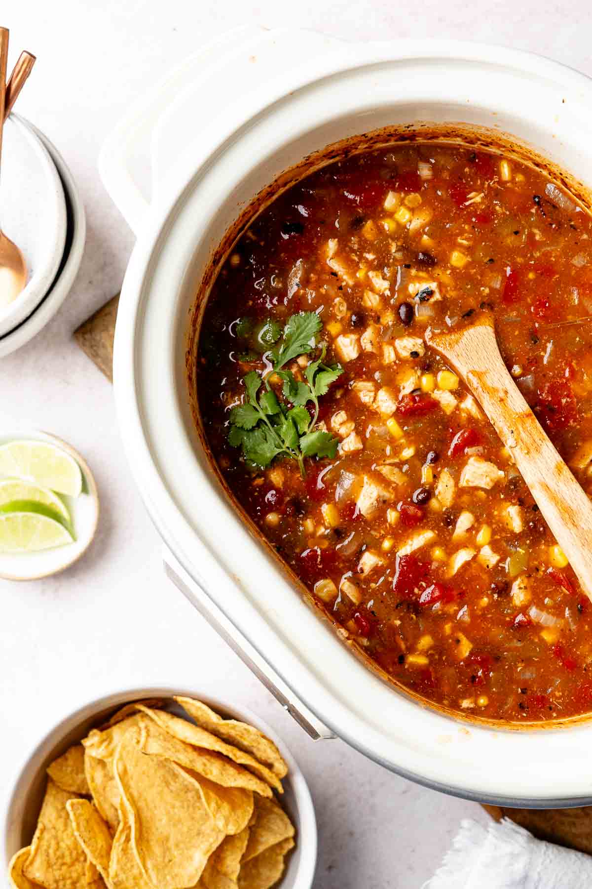 Chicken tortilla soup in slow cooker, wooden spoon resting in soup.