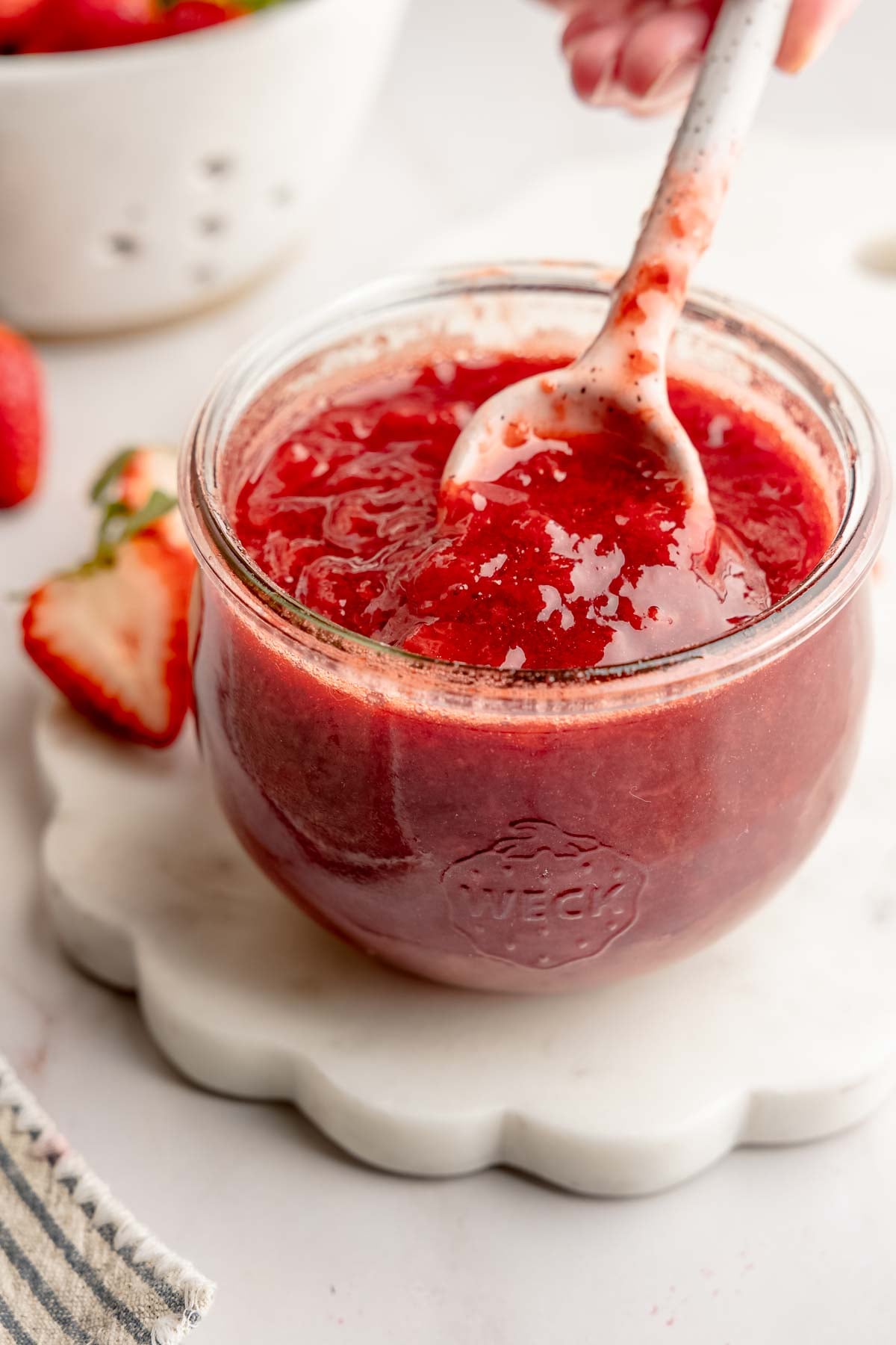 Weck jar filled with strawberry fruit sauce, ceramic spoon lifting sauce.