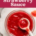 Overhead view of jar full of strawberry fruit sauce with ceramic spoon lifting the sauce from the jar.