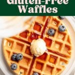 Overhead view of gluten-free waffles garnished with butter and blueberries, is drizzled with syrup.