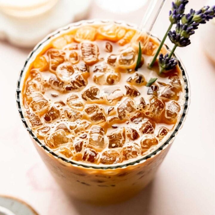 Iced lavender oat milk latte in glass garnished with lavender sprigs.