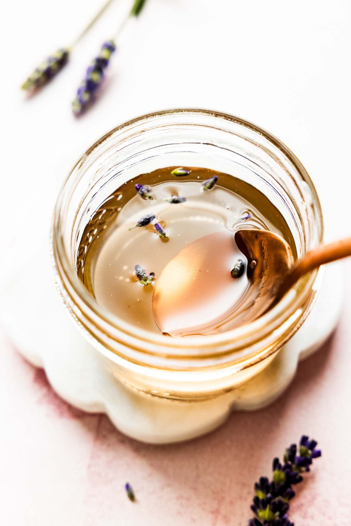 Close-up overhead shot of golden lavender syrup in a jar with a spoon.