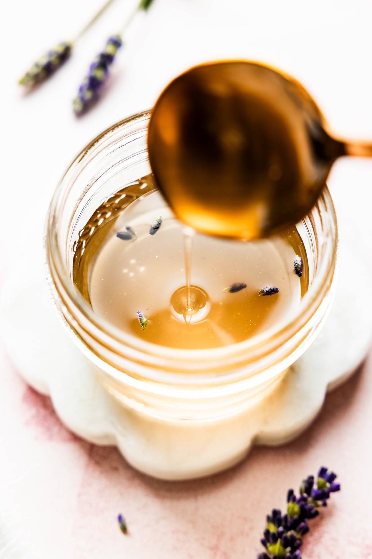 Golden lavender syrup drizzling from a copper spoon into a glass jar.