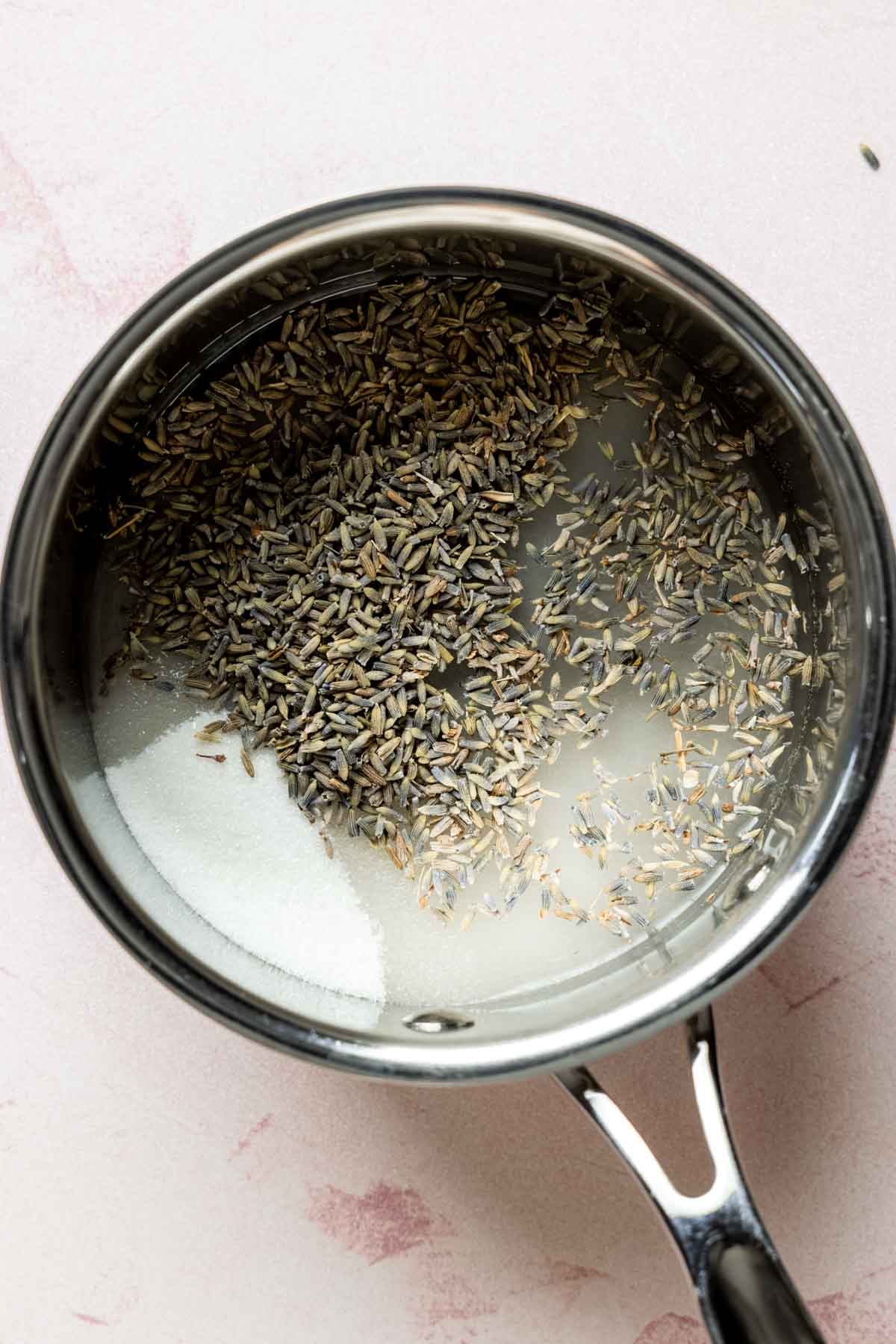 Saucepan with dried lavender buds, granulated sugar, and water before cooking.