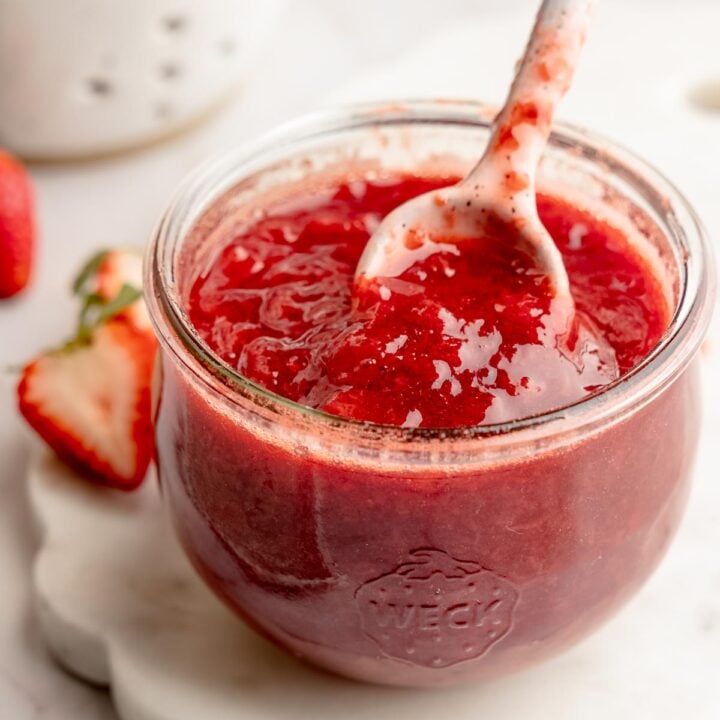 Weck jar filled with strawberry fruit sauce, ceramic spoon lifting sauce.
