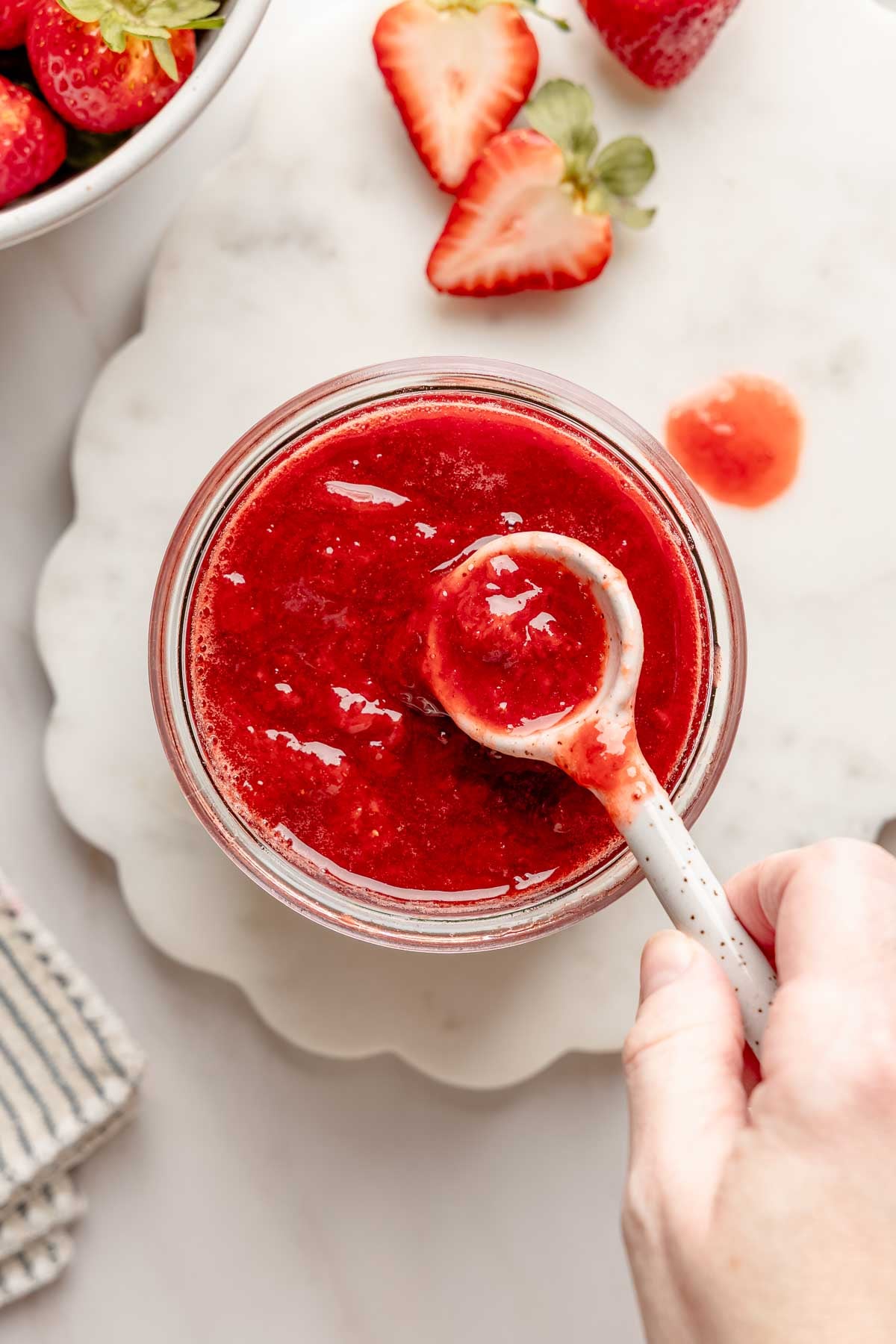 Overhead view of jar full of strawberry fruit sauce with ceramic spoon lifting the sauce from the jar.