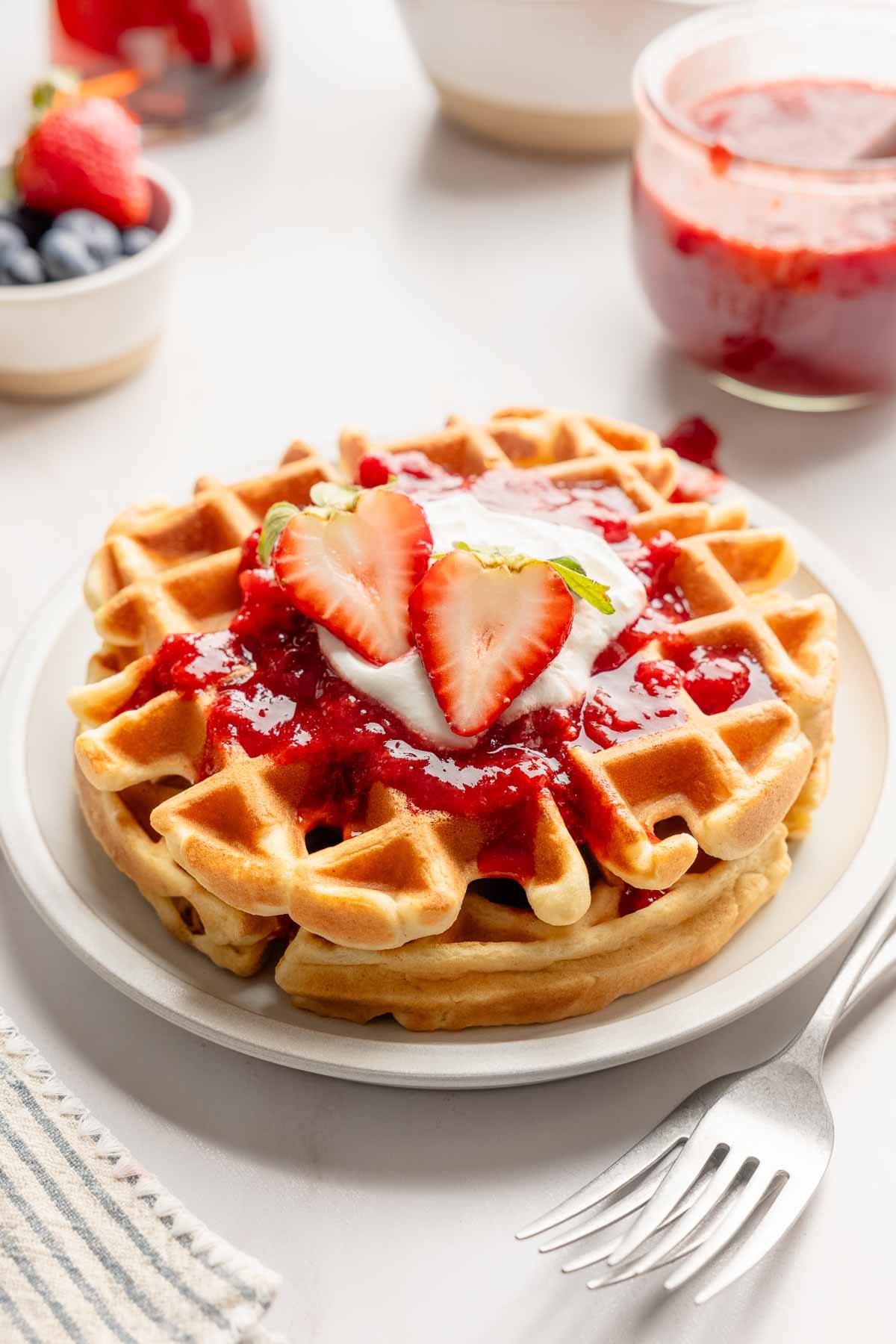 Two Belgian waffles topped with strawberry sauce, whipped cream and strawberry cut in half. 