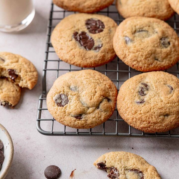 Almond flour chocolate chip cookies on wire rack next to glass bottle of milk.