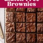 Fudgy gluten-free brownies sliced into squares and arranged on parchment paper, on wire rack next to knife.
