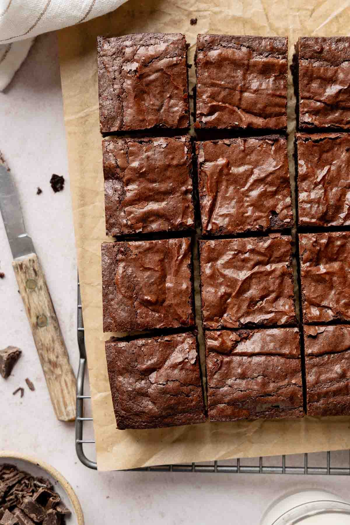 Gluten-Free Brownies sliced into squares, resting on parchment paper and a wire rack next to a knife.