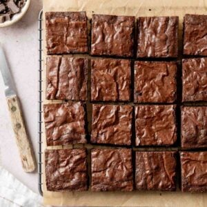 Fudgy gluten-free brownies sliced into squares and arranged on parchment paper, on wire rack next to knife.