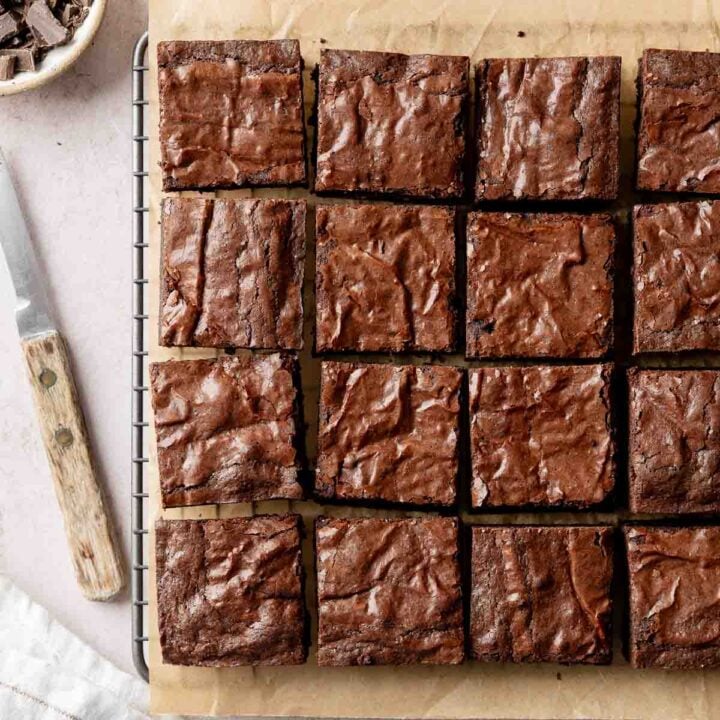 Fudgy gluten-free brownies sliced into squares and arranged on parchment paper, on wire rack next to knife.