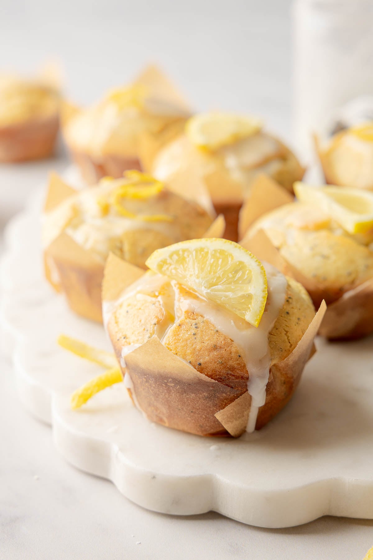 Lemon poppy seed muffins with glaze and lemon slice garnish on marble board.