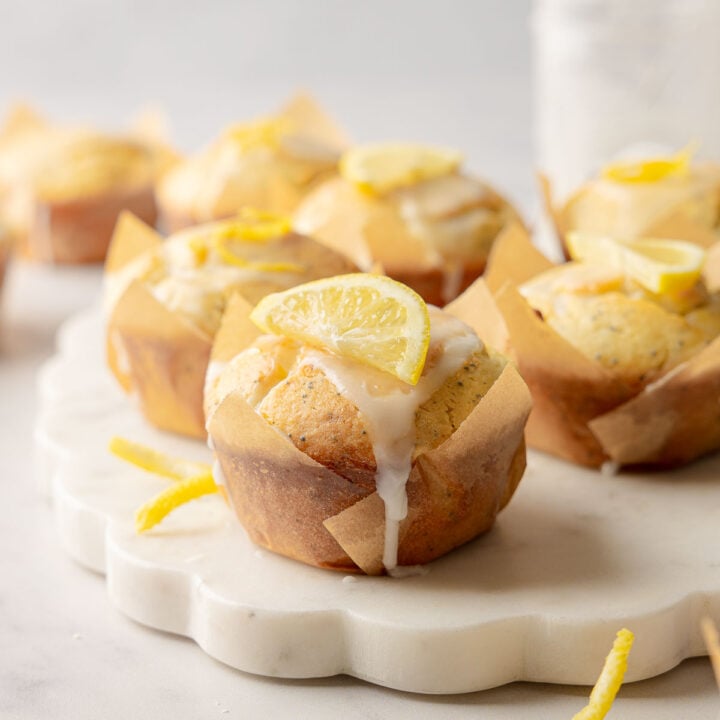 Lemon poppy seed muffins with glaze and lemon slice garnish on marble board.