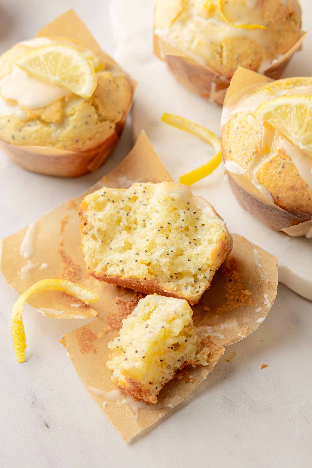Halved lemon poppy seed muffin showing moist crumb with glaze and zest on parchment.