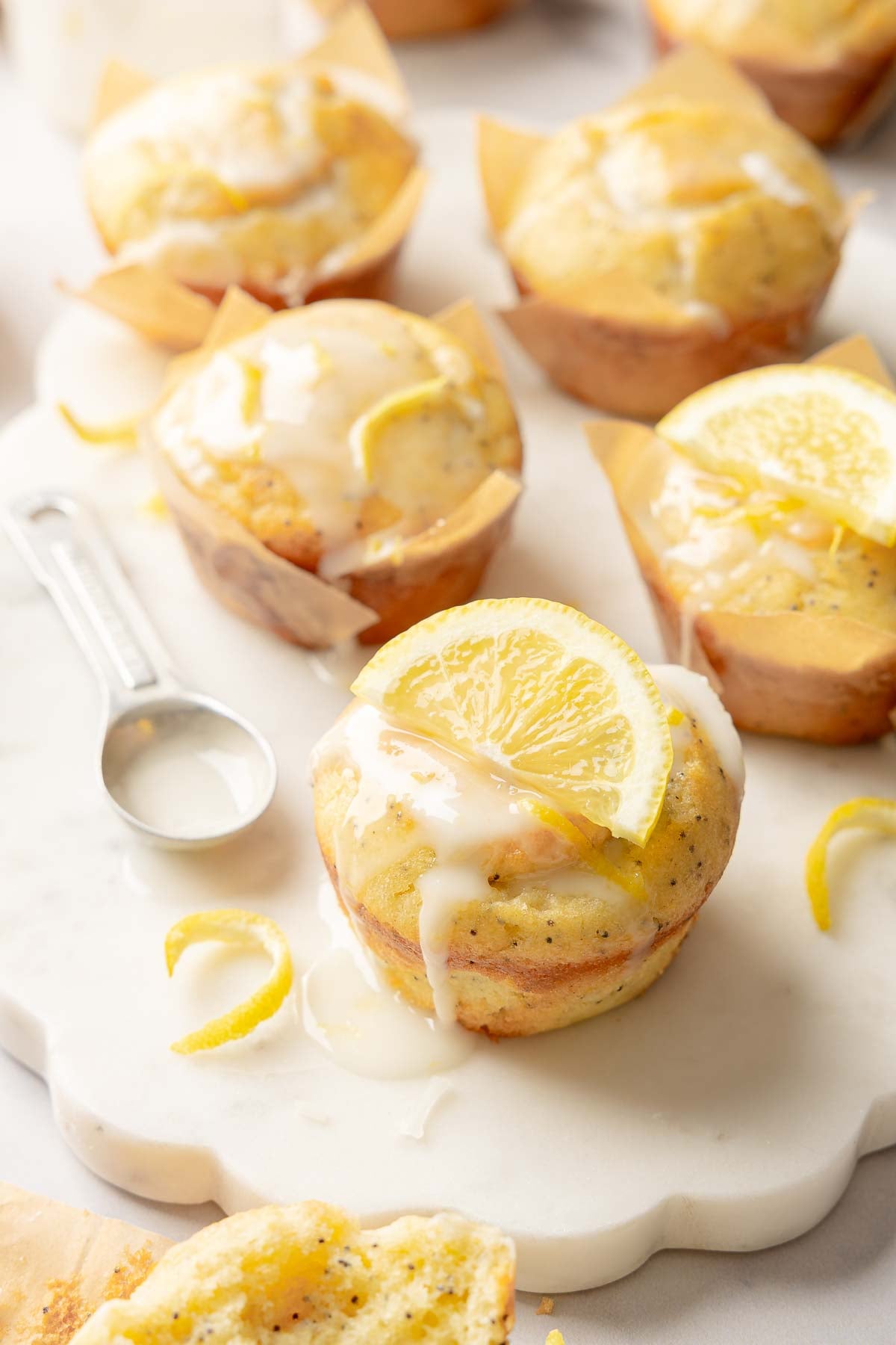 Glazed lemon poppy seed muffins topped with lemon slices, served on marble board with zest.