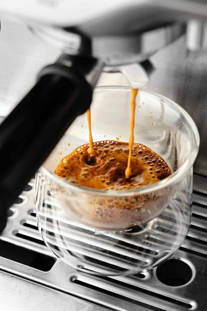 A shot of espresso pouring from portafilter into espresso glass.