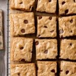 Squares of gluten-free blondies studded with chocolate chips on wire rack.