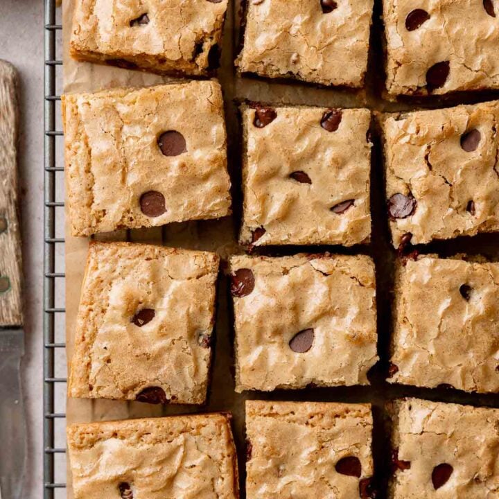 Squares of gluten-free blondies studded with chocolate chips on wire rack.