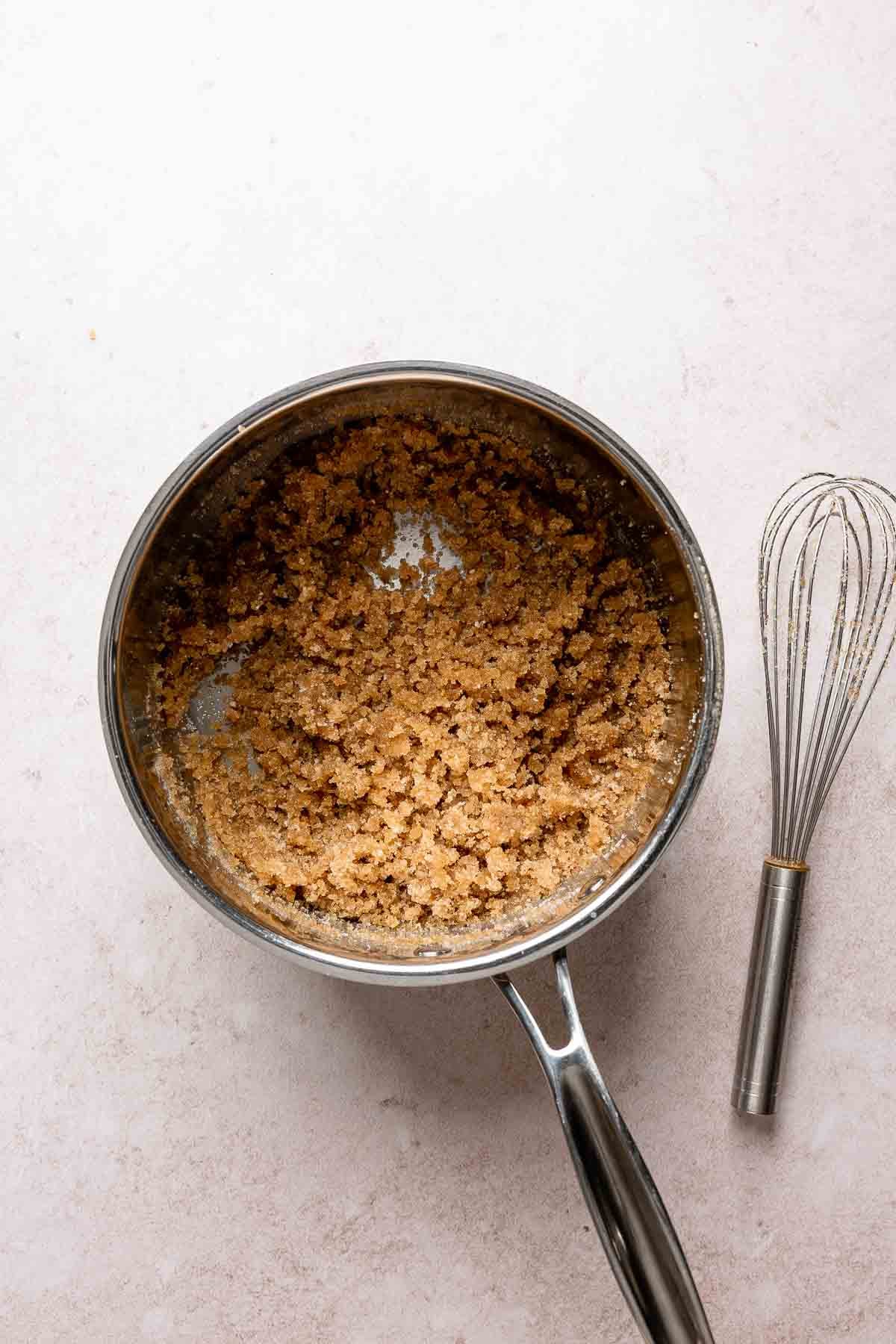 Brown butter mixed with brown sugar in saucepan beside whisk.