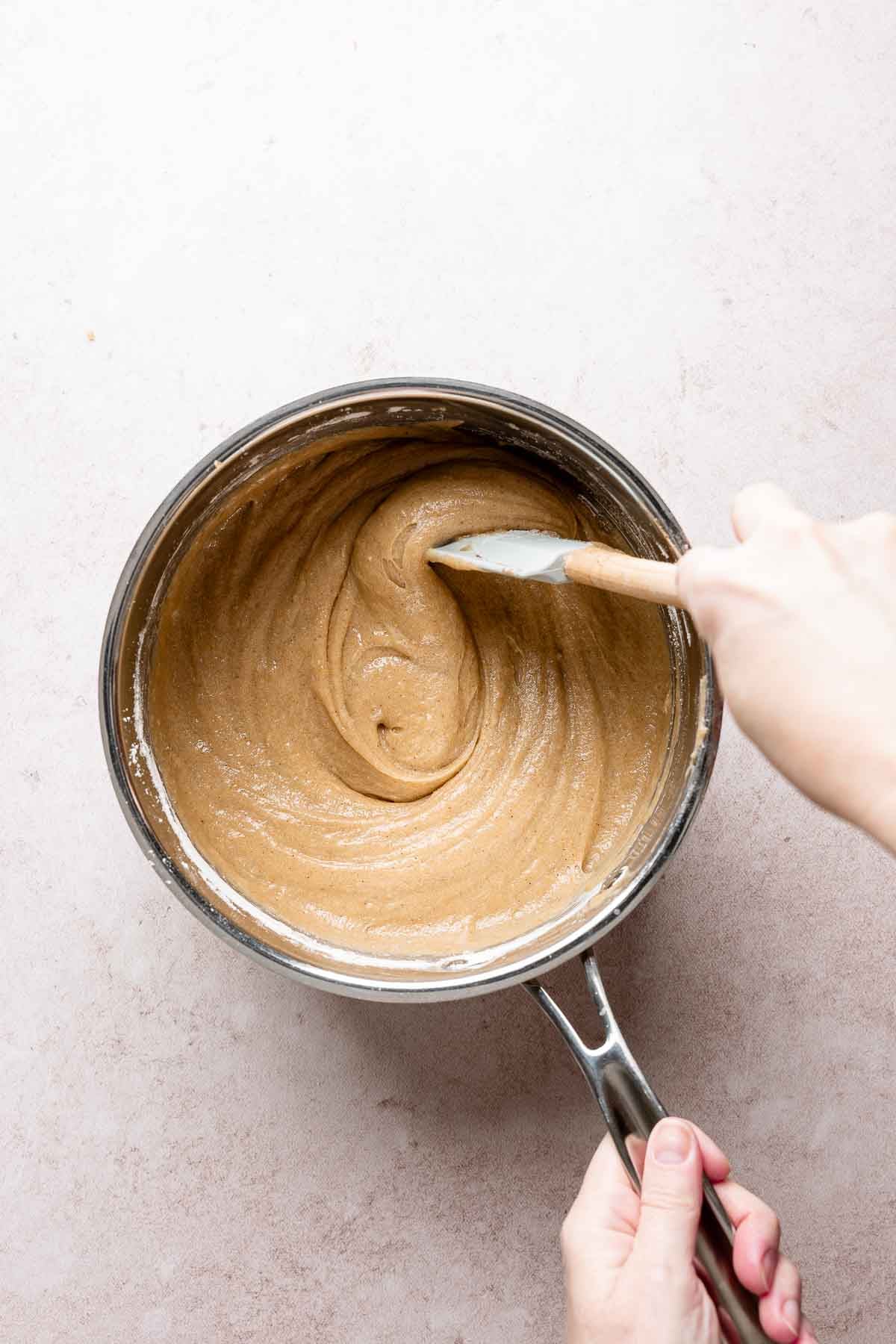 Flour stirred into blondie batter with spatula in saucepan.
