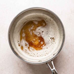 Brown butter with deep golden toasted milk solids visible beneath the foam in a saucepan.