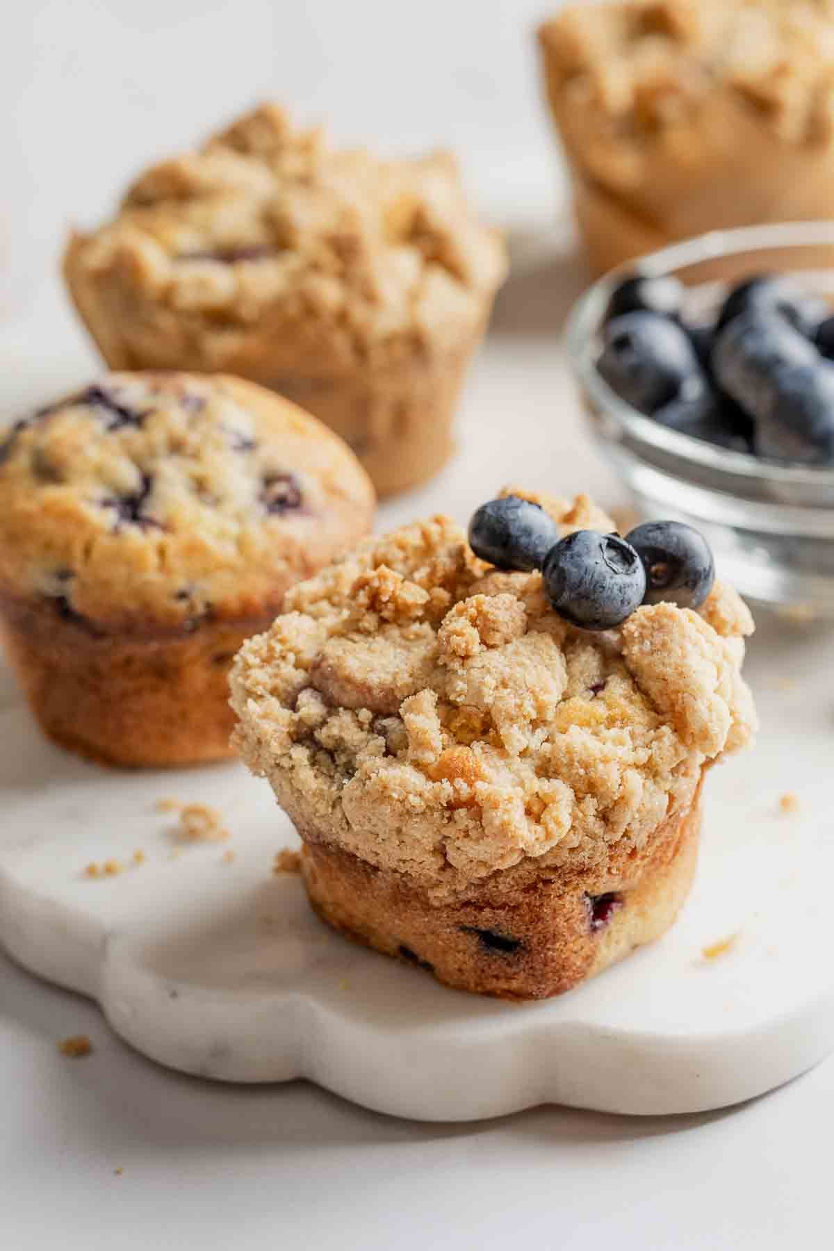 Gluten-free blueberry muffins with streusel and garnished with fresh blueberries, on marble platter.