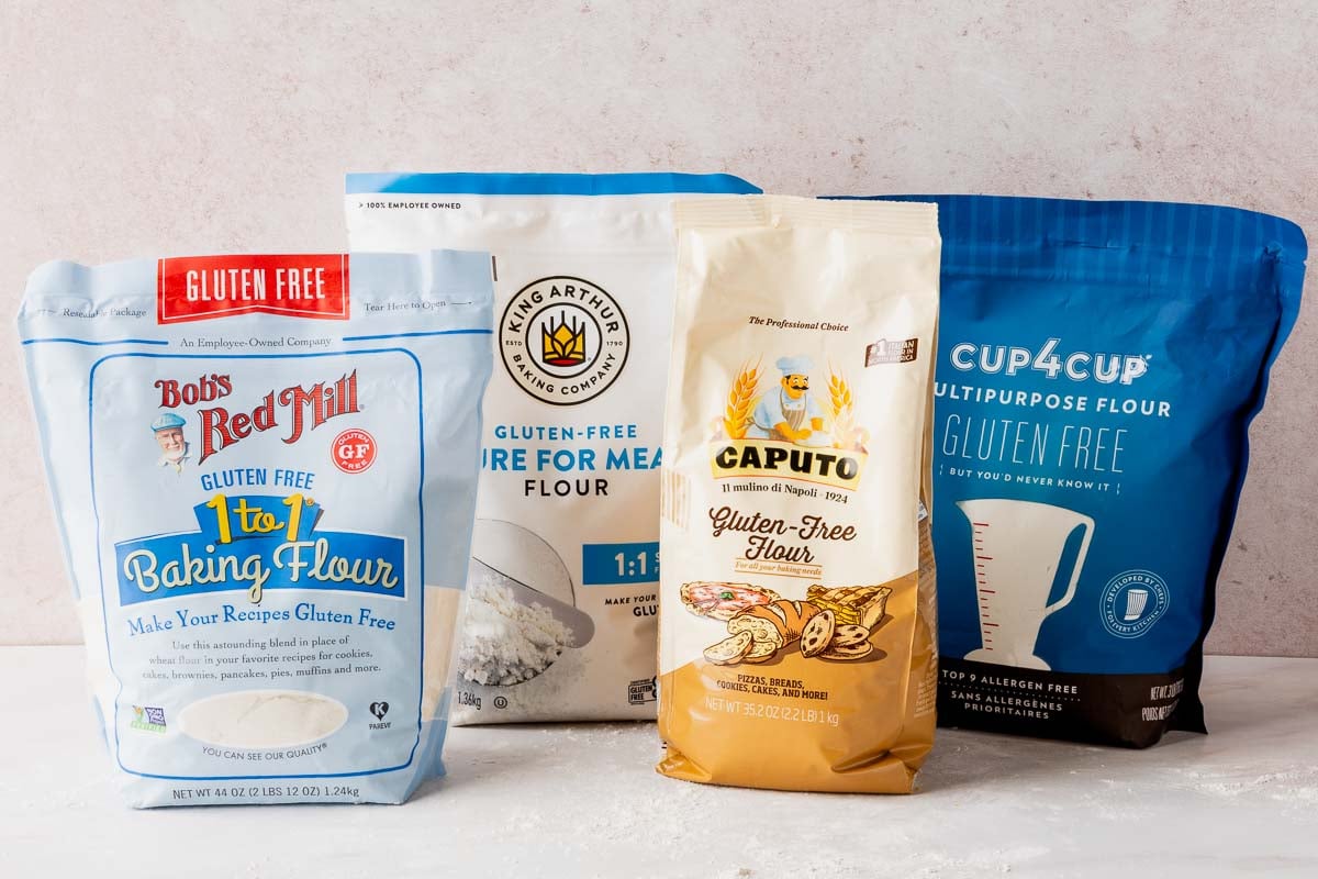 Bob's Red Mill, King Arthur, Caputo Fioreglut, and Cup4Cup gluten-free flours in bags on pink surface.