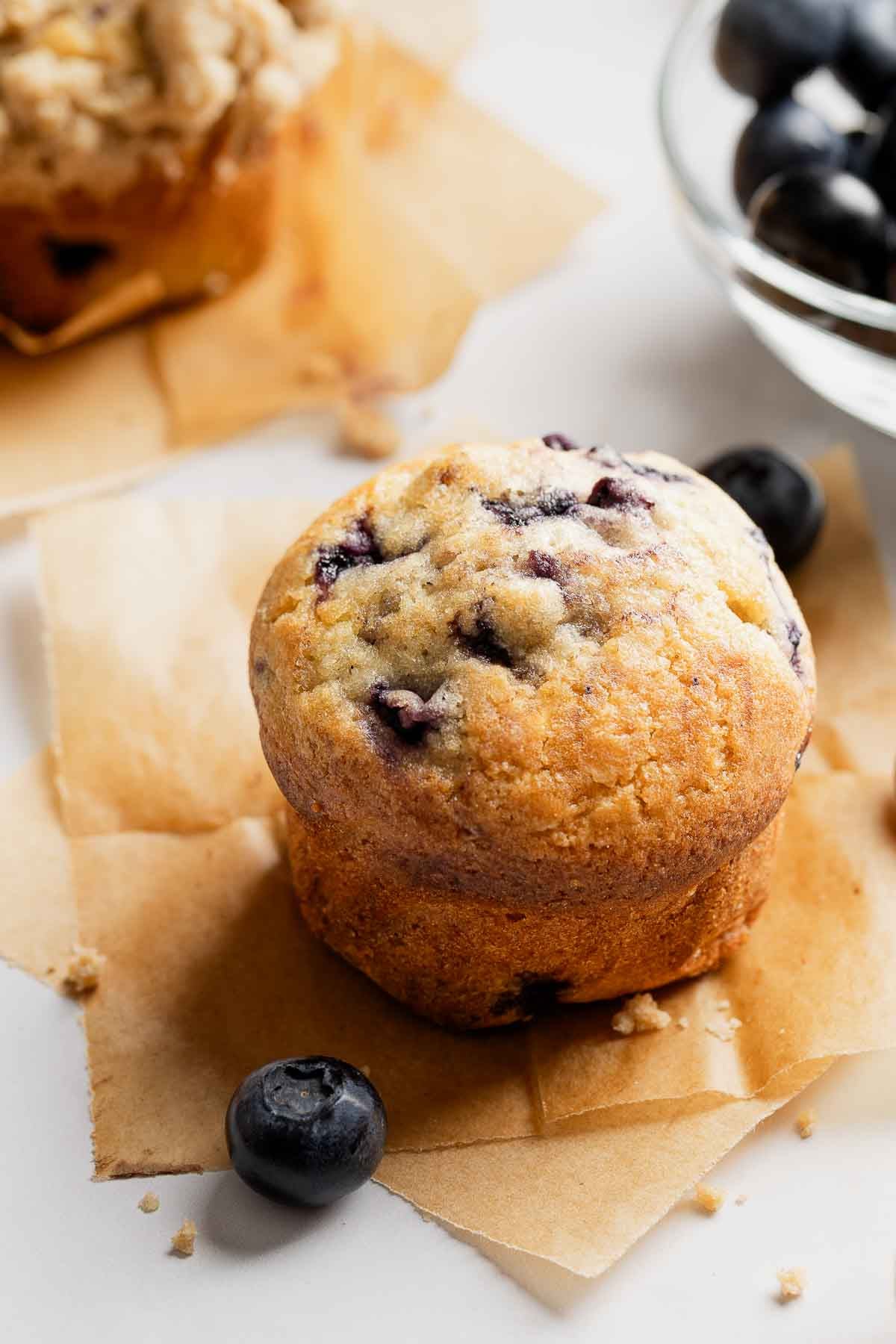 Blueberry muffin on parchment paper squares, next to fresh blueberries.