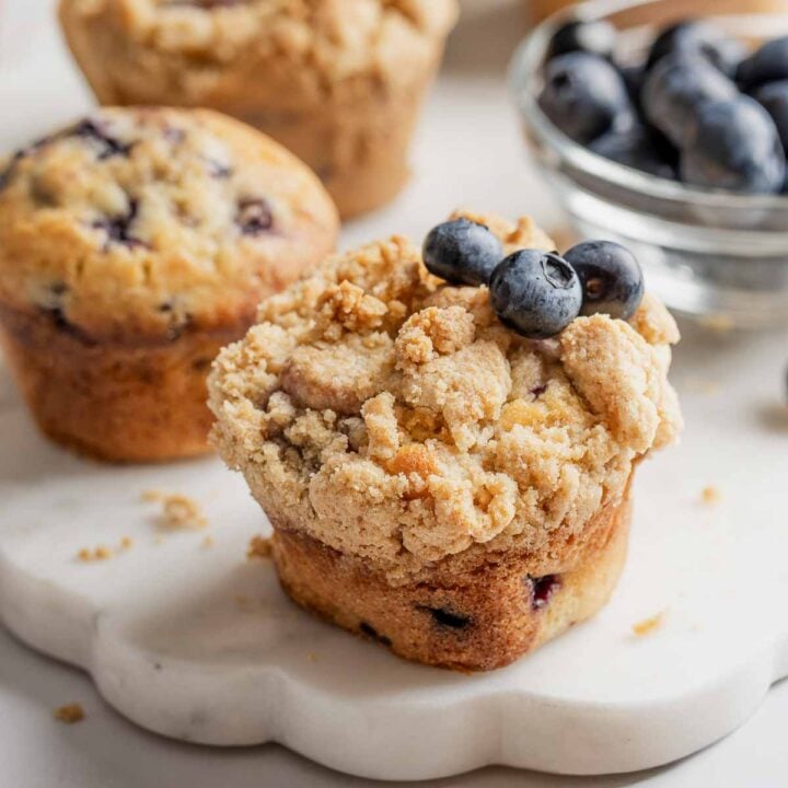 Gluten-free blueberry muffins with streusel and garnished with fresh blueberries, on marble platter.