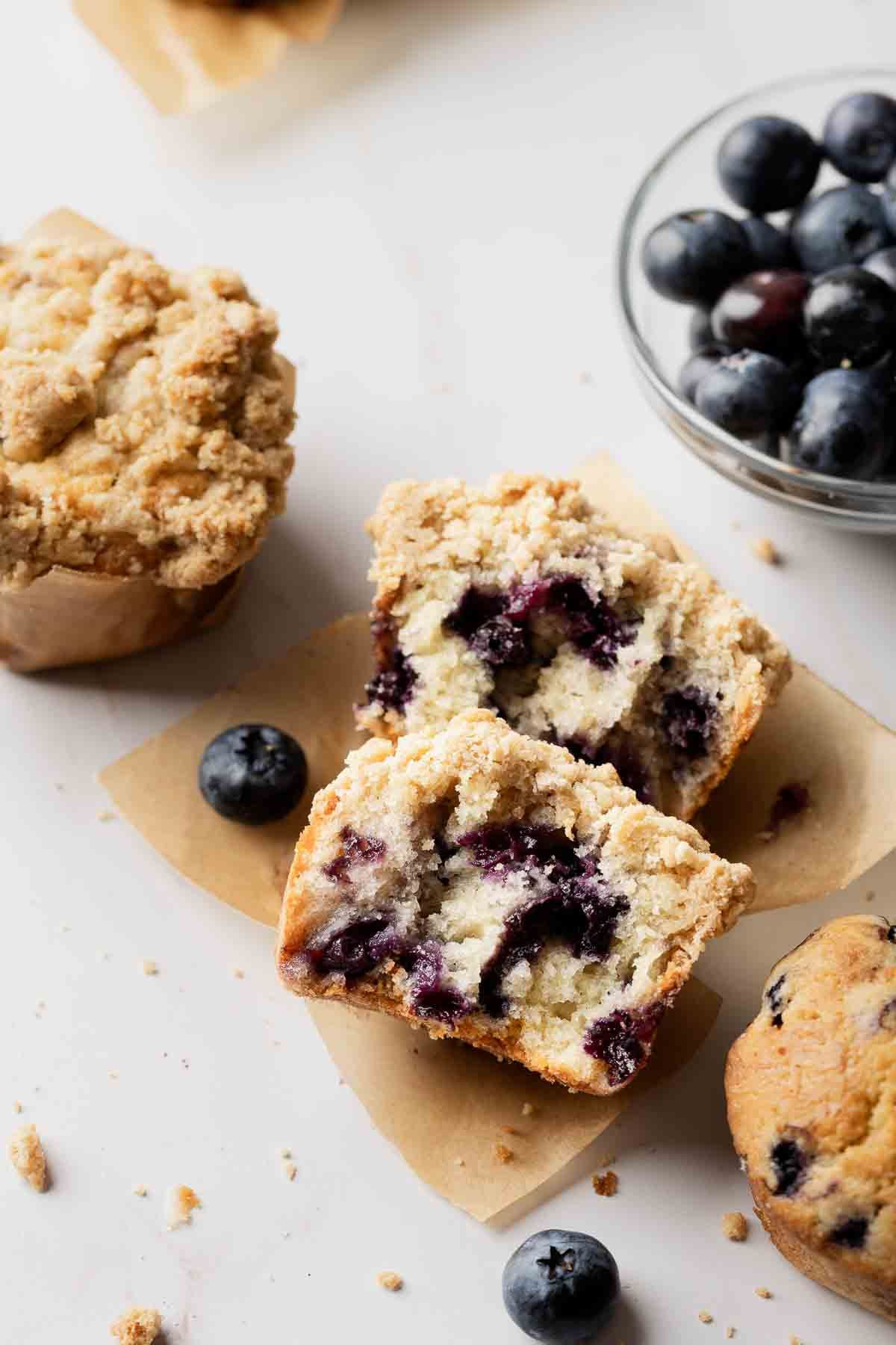 Blueberry muffin on parchment paper, split in half to show soft texture filled with juicy blueberries.