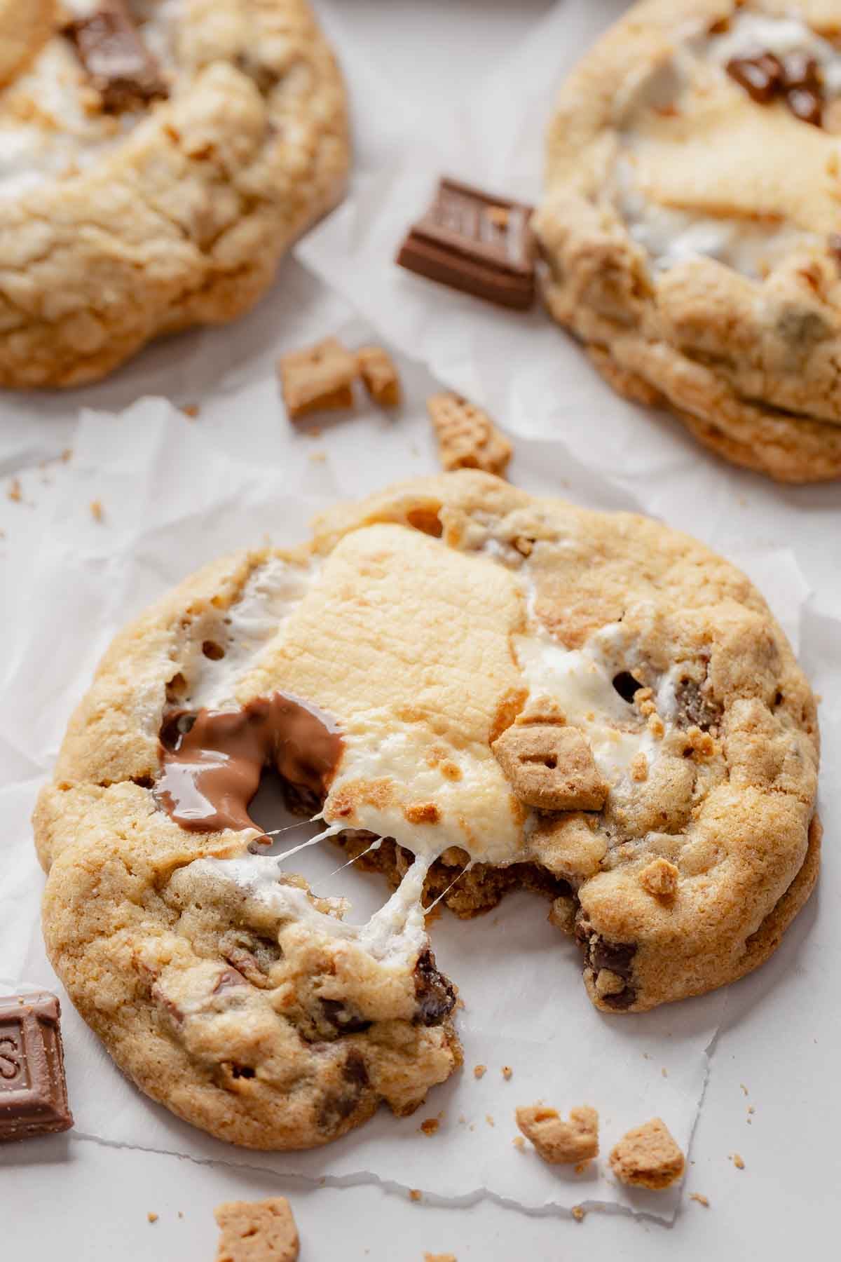 Gluten-free s'mores cookie on parchment paper, pulled apart showing gooey marshmallow and melty chocolate.