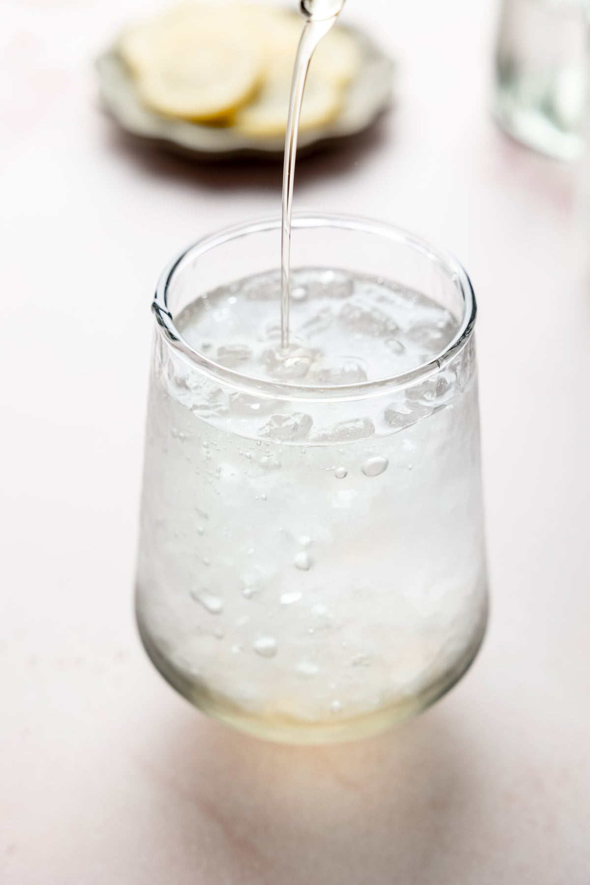 Sparkling mineral water being poured over ice in a glass to make a sparkling Americano.