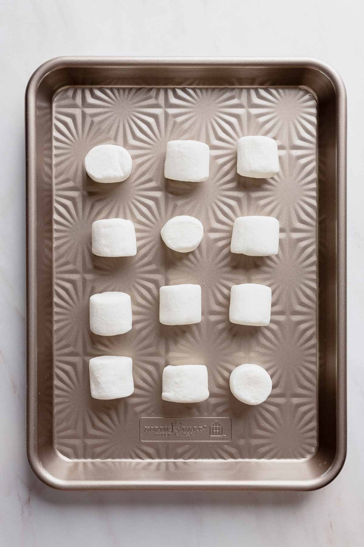 Twelve marshmallows on a baking sheet, ready to go into the freezer.